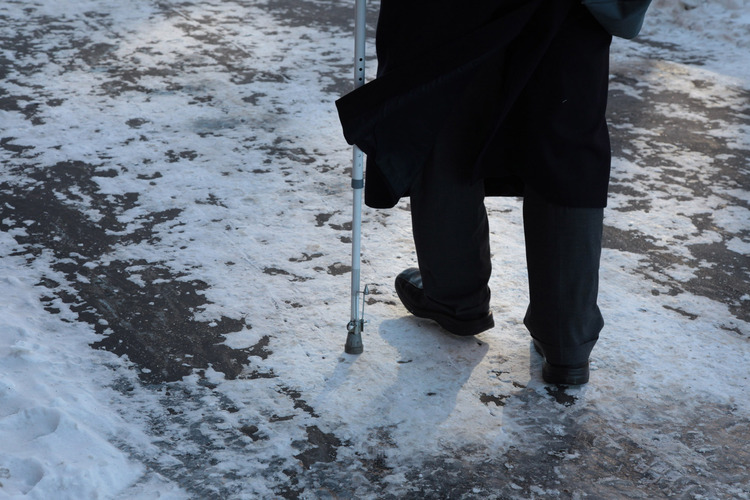 Ihminen kävelee talvisella tiellä kävelykeppiin tukeutuen