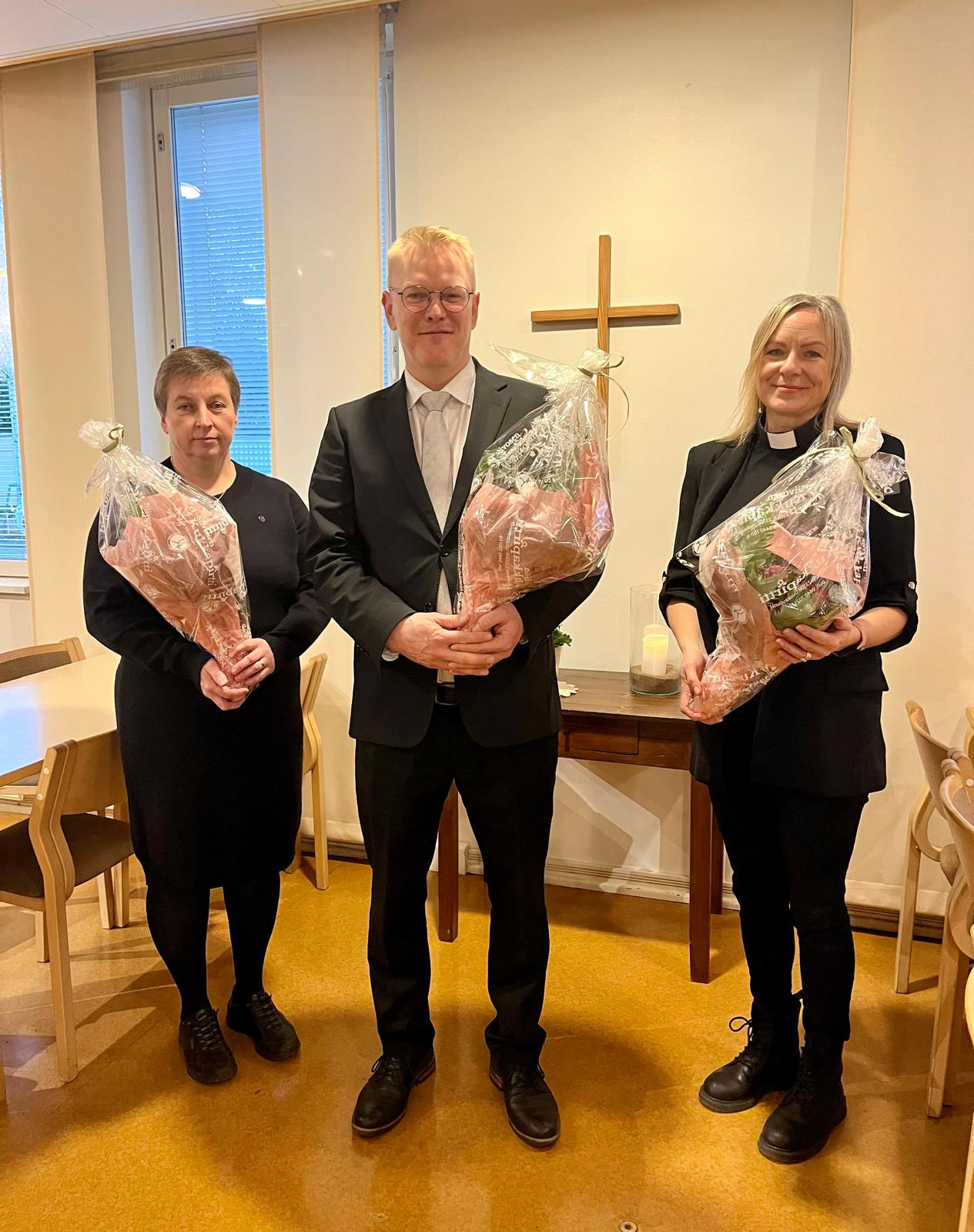 Tehtäviin siunatut poseeraavat seurakuntakeskuksella ristin edessä ja kukat käsissään.